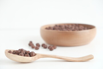 Chocolate corn balls in a wooden bowl and spoon on a white background. Copy, empty space for text