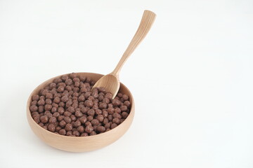Chocolate corn balls in a wooden bowl and spoon on a white background. Copy, empty space for text