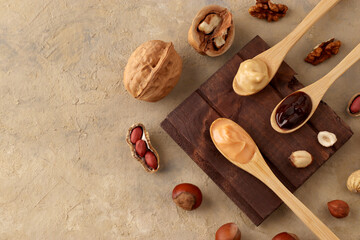 Concept for natural and vegetarian products. Butter, nut paste in wooden spoons with ingredients on a light background. Homemade Raw Organic Hazelnut, Peanut, Walnut. Top view, flatlay. Copy space.