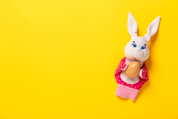 Banner with white bunny and egg in hand on yellow background with copy space, empty text place. Christian holiday card Happy Easter. Online toy theater course. Hand puppet. Traditional childhood play