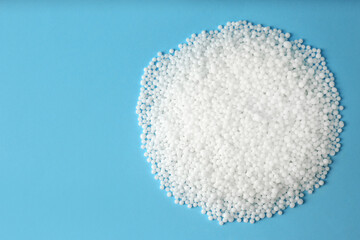Pellets of ammonium nitrate on light blue background, flat lay with space for text. Mineral fertilizer