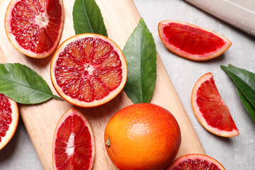Ripe red oranges, green leaves and wooden board on light table, flat lay