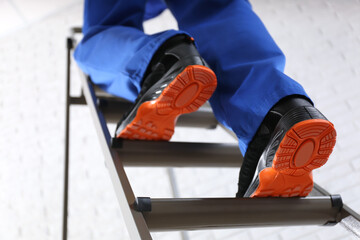 Professional worker climbing up ladder indoors, low angle view