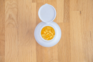 White jar with yellow transparent capsules of fish oil (omega-3, vitamin E) stands on a wooden table top view. Supplements and vitamins for sports and health in daily life