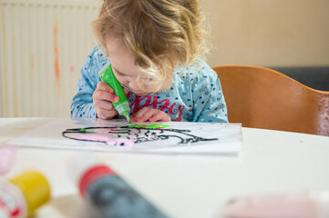 Cute girl drawing a fish using glass colors at home.