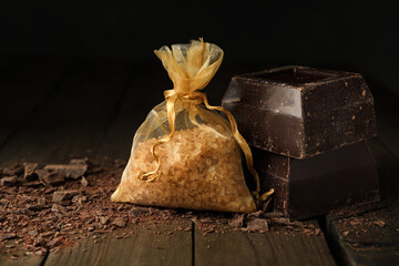 Scented sachet with aroma beads and dark chocolate on wooden table, closeup