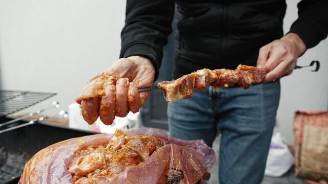 Male hands take raw meat shish kebab and string it on metal skewers.