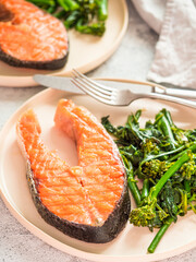 Ready-to-eat grilled salmon steak and greens - baby broccoli or broccolini and spinach on rustic craft plate over gray background. Keto diet dish. Vertical