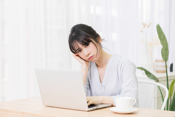 部屋でノートパソコンを使いながら悩む女性