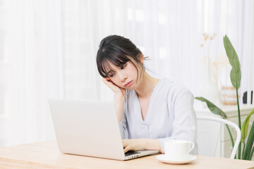 部屋でノートパソコンを使いながら悩む女性