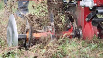 Agriculture works, plowing field before planting. Above view of slow motion of thickened knives of agricultural cultivator digging ground and grass in the garden. The soil is flying from blades.