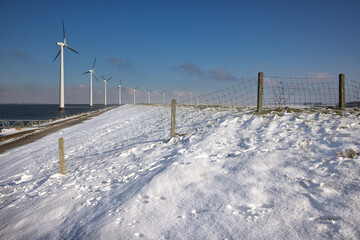 Fototapeta na wymiar Row offshore windturbines along Ductch coast in winter with snow
