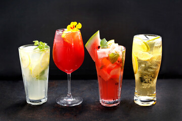 Composition of colorful lemonades, drinks, cocktails in various glasses, on a black stony background.