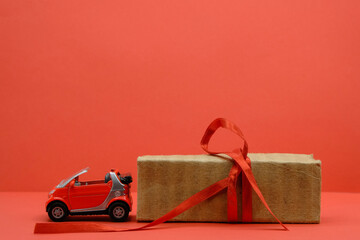 Red small car toy near the unpacked box with a red ribbon. Red background. Gift, surprise concept. Buy car concept. Copy space.