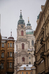 Mostecka Street with a view of the Church of Saint Nicholas, old town with historical buildings, snow in winter day, Mala Strana or Lesser Town district, Prague, Czech Republic