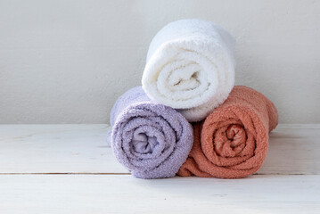 Fototapeta na wymiar Three clean terry multi-colored towels orange, white and purple folded in a roll