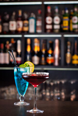 Blue and red cocktails on the bar. Alcoholic cocktails on a background of shelves with bottles. Blurred bottles of alcohol on the wall of the bar.