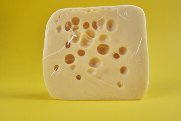 Cheddar cheese in plastic packaging is on a yellow background