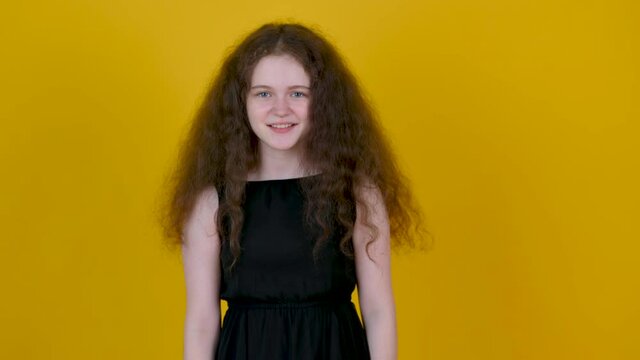 Happy young girl with curly hair posing isolated on yellow background. People emotions lifestyle concept. Girl tenager doing winner gesture