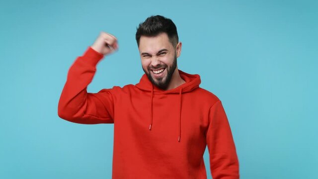 Happy overjoyed young man 20s years old in red streetwear hoodie isolated on blue background studio. People lifestyle concept. Count countdown 1 2 3 one two three doing winner gesture clenching fists
