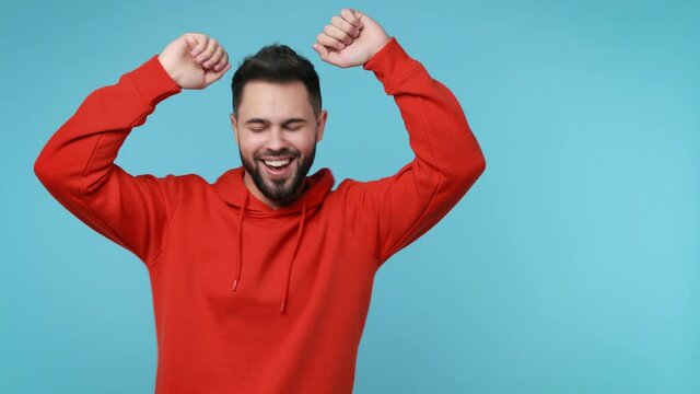 Cheerful funny young man 20s years old in red streetwear hoodie isolated on blue background studio. People lifestyle concept. Doing dab hip hop dance hands move gesture youth sign hiding covering face