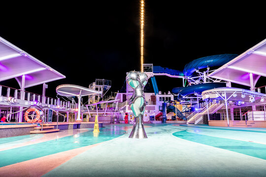 At Sea - October 11 2019: Empty Open Top Deck Onboard Norwegian (NCL) Cruise Ship  With Metallic Sculpture. No People On Dance Floor For Night Entertainment. Waterslide And Clear Sky In Background.