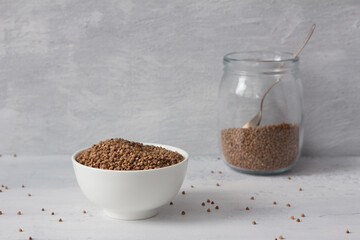 Raw buckwheat in a white ceramic bowl on a light gray textured background, free space