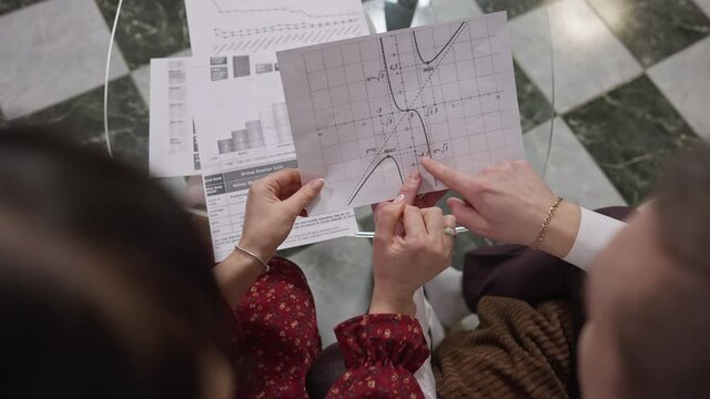 Top view of graphs with male and female Caucasian hands gesturing in slow motion. Shooting over shoulder of unrecognizable man and woman discussing startup project indoors.