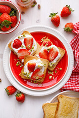 Toasts with creamy cheese, fresh strawberries and pistachios on a ceramic plate, top view. An idea for a delicious breakfast or dessert.