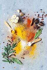 Various spice powders (paprika, curry, coriander, ginger, dried onions and garlic, turmeric, cinnamon, pepper, anise) and herbs (rosemary, bay leaf) on a blue background. Indian and Asian cuisine.