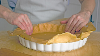 The process of making a base for a shortcrust quiche pie, male hands transfer a rolled dough sheet into a baking dish. Authentic home hobby home baker. Pie crust recipe