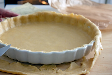 The process of making a base for a shortcrust quiche pie, male hands transfer a rolled dough sheet into a baking dish. Authentic home hobby home baker. Pie crust recipe
