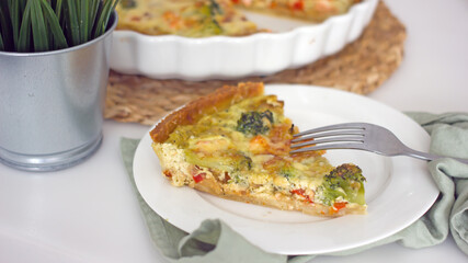 A French quiche pie in a baking dish on the kitchen table is cut into pieces with a knife. Homemade authentic baking with your own hands