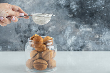 Female hand sprinkling a sugar powder on a walnut shaped cookies
