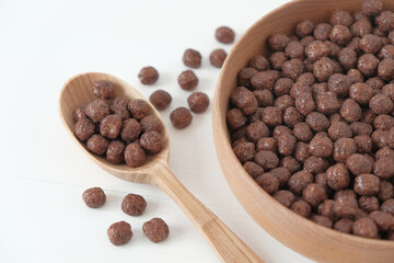 Chocolate corn balls in a wooden bowl and spoon scattered on a white background. Top view. Copy, empty space for text