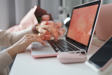 Female hands using laptop. Female office desk workspace homeoffice mock up with laptop, pink tulip flowers bouquet, smartphone and pink accessories