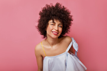 Fashionable lady with curly brunette hair in stylish dress looking into camera on pink background