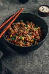 Fried Rice with vegetables, green onion and sesame in black bowl on stone background.