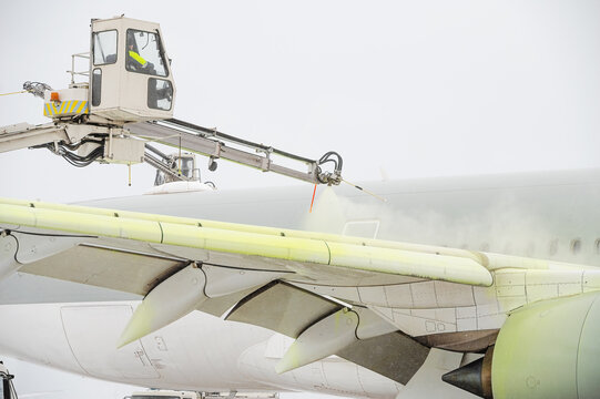 Winter at the airport. Snow storm. Airplane de-icing before take off. De-icing the aircraft before the flight. The de-icing machine sprinkles the wing of a passenger plane with de-icing fluid.