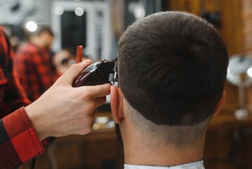 Making haircut look perfect. Young bearded man getting haircut by hairdresser while sitting in...
