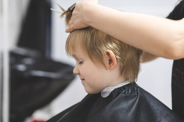 Hairdresser cuts hair happy smiling blond child boy. Lifestyle close-up. Concept of beauty, hygiene.