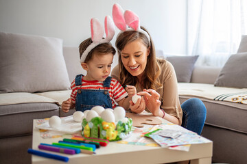 Mother and son painting Easter eggs. Preparing for Easter. Mother and son paint eggs. Family at home. Happy family preparing for Easter. Cute little child wearing bunny ears on Easter day.