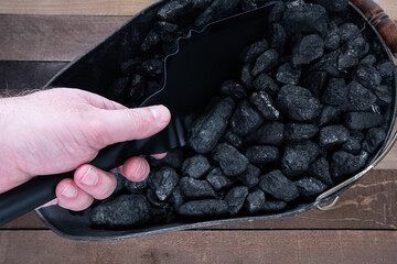 A hand with a shovel digging out anthracite nut coal from a coal scuttle