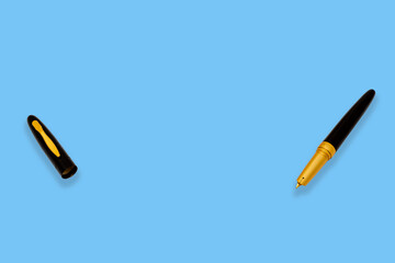 Top-down view - open black gold-tipped fountain pen, cover on the left, blue background, space for text.