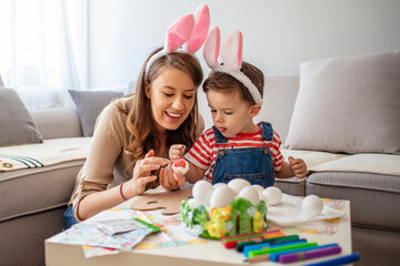 Happy easter! A mother and her son painting Easter eggs. Happy family preparing for Easter. Cute little child boy wearing bunny ears on Easter day. Mother And Son Enjoying Creative Day