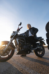 Fototapeta na wymiar white caucasian man blond long hair biker riding a motorcycle with leather jacket and white t-shirt with wheels in scrapyard with sunset light
