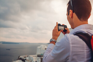 Obraz premium Santorini traveler man taking photo of Caldera in sea from Oia, Greece on camera. Tourism, traveling, summer vacation