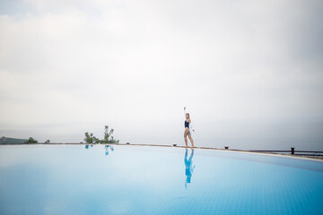Naklejka premium Beautiful woman in black swimsuit posing near outdoor pool with sea view