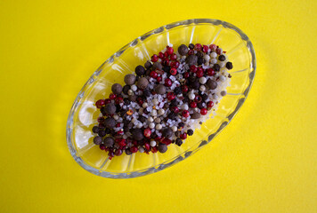 Spices, white, black and red peppers, sea salt on glass plate on a yellow background, close-up