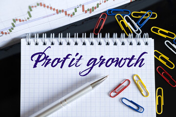 On the desktop are a forex chart, paper clips, a pen and a notebook in which it is written - Profit growth